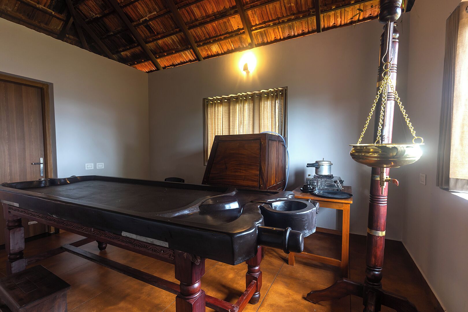 A billiards table in a room with a wooden ceiling, a traditional scale, and a window with curtains.