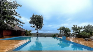 A rectangular swimming pool with a wooden deck, surrounded by trees and a view of distant hills. - Sandal Mist Resort and spa  (Kasaragod)