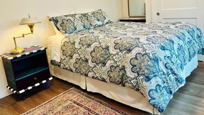 Ein Schlafzimmer mit einem geblümten Bettüberwurf, einer Nachttischlampe, einem Nachttisch und einem Teppich.