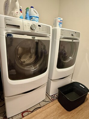 Deux machines à laver à chargement frontal, avec des bouteilles de lessive et un panier à linge.