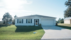 A single-story house with a front garage, a well-maintained lawn, and a clear sky. - Welcome to your Serene Retreat.  (Palm Bay)