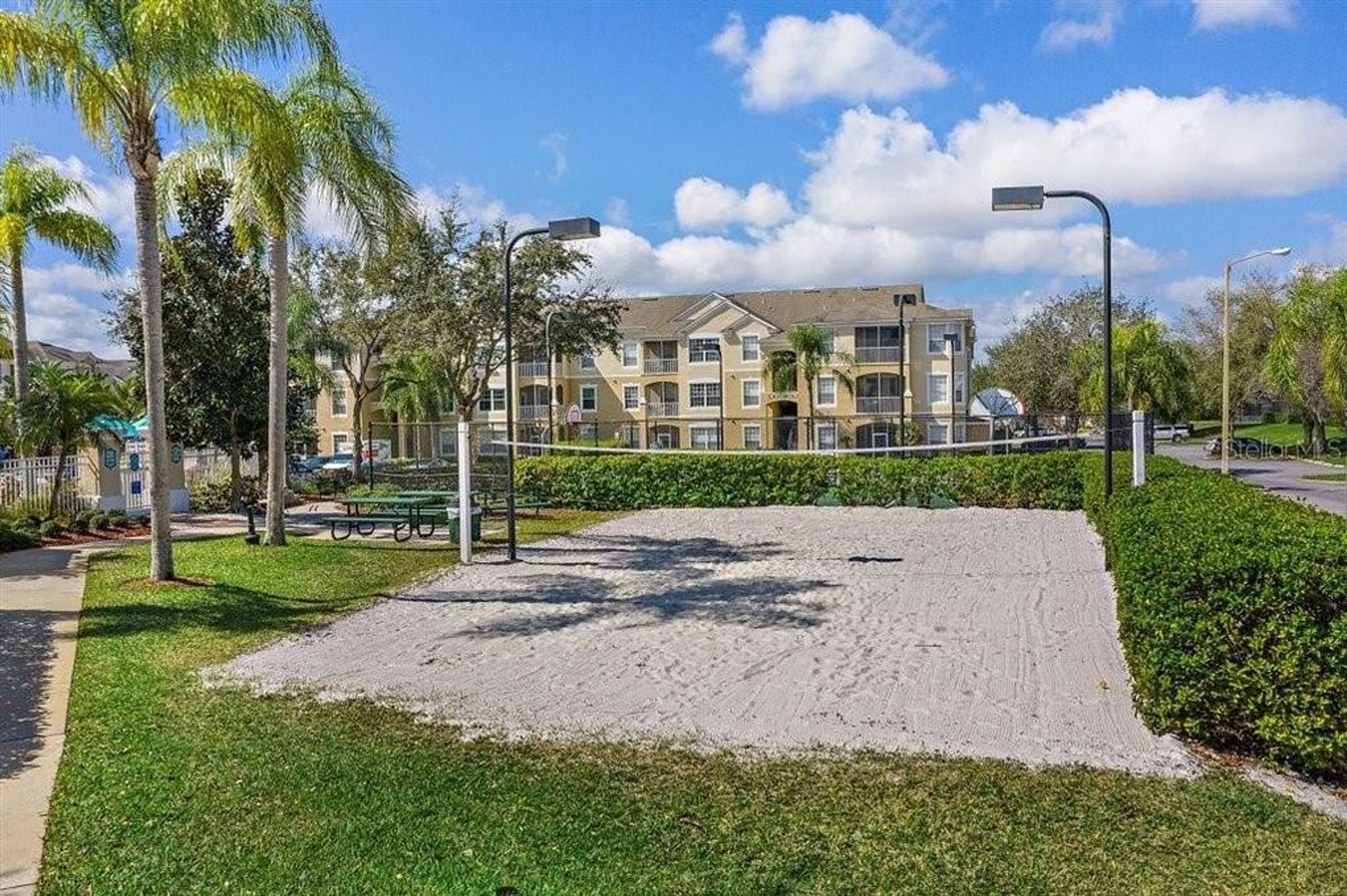 Um edifício residencial com um pátio arenoso, cercado por vegetação e palmeiras.