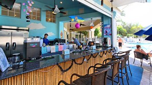 An outdoor bar area with a counter, seating, and a pool in the background. - 4 Bed in Windsor Palms Resort - Steps to Disney (Kissimmee)