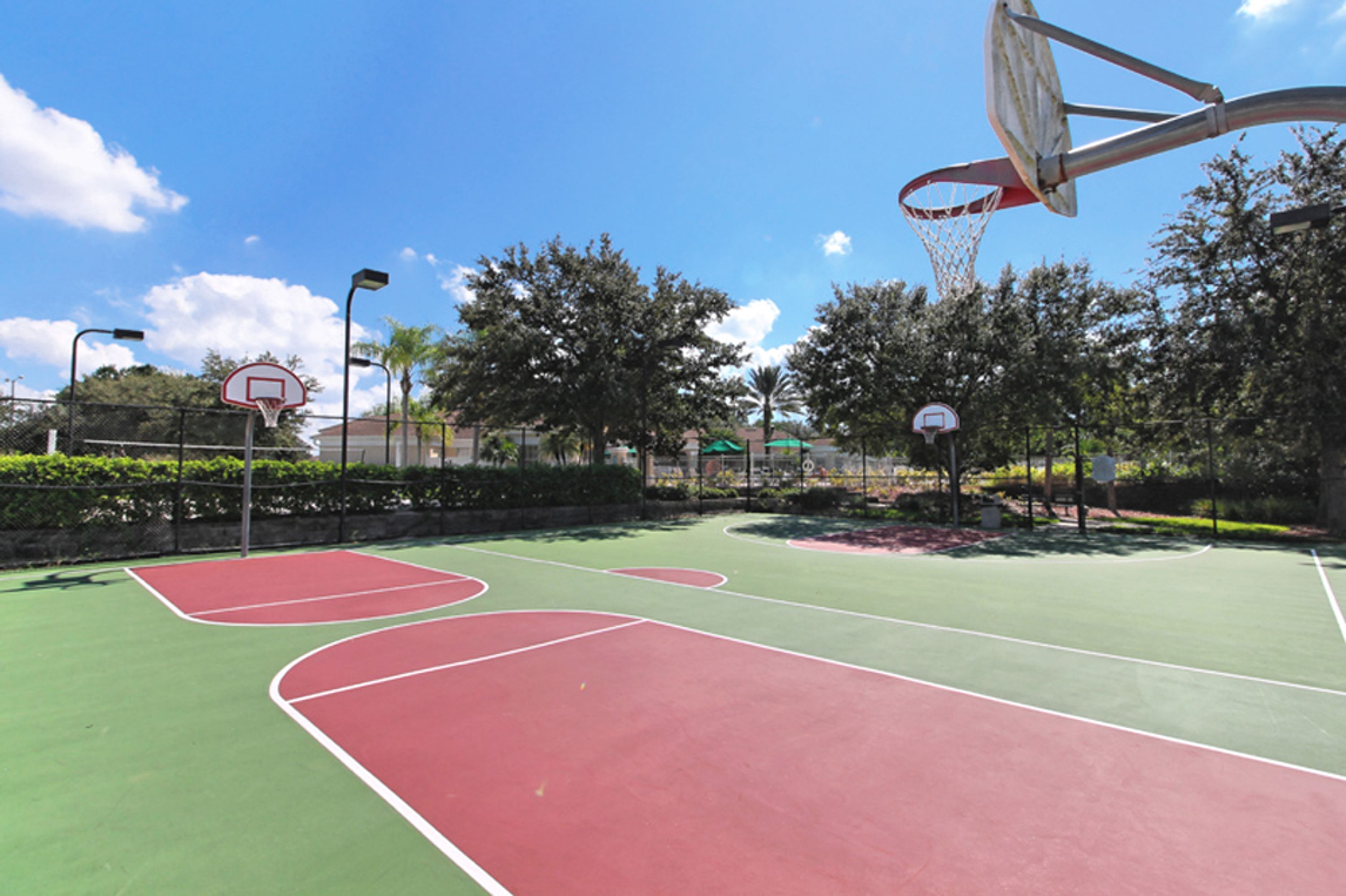 An outdoor basketball court with multiple hoops, surrounded by trees and a clear sky.