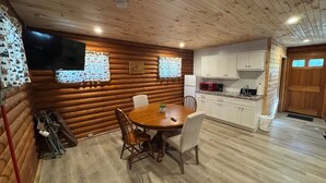 A cozy log cabin interior with a dining area, kitchen, and a wooden door. - Adorable log cabin on back country road with peace, quiet, all amenities of home (Kimbolton)