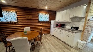 A cozy log cabin interior with a wooden dining table, chairs, a kitchen with white cabinets, and a microwave. - Adorable log cabin on back country road with peace, quiet, all amenities of home (Kimbolton)