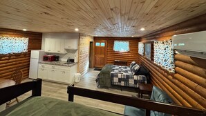 A log cabin interior with a kitchen, dining area, and a bed. - Adorable log cabin on back country road with peace, quiet, all amenities of home (Kimbolton)