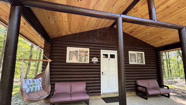 A cabin with a porch, two cushioned seating areas, a swing chair, and a door marked with the number 4. - Adorable log cabin on back country road with peace, quiet, all amenities of home (Kimbolton)