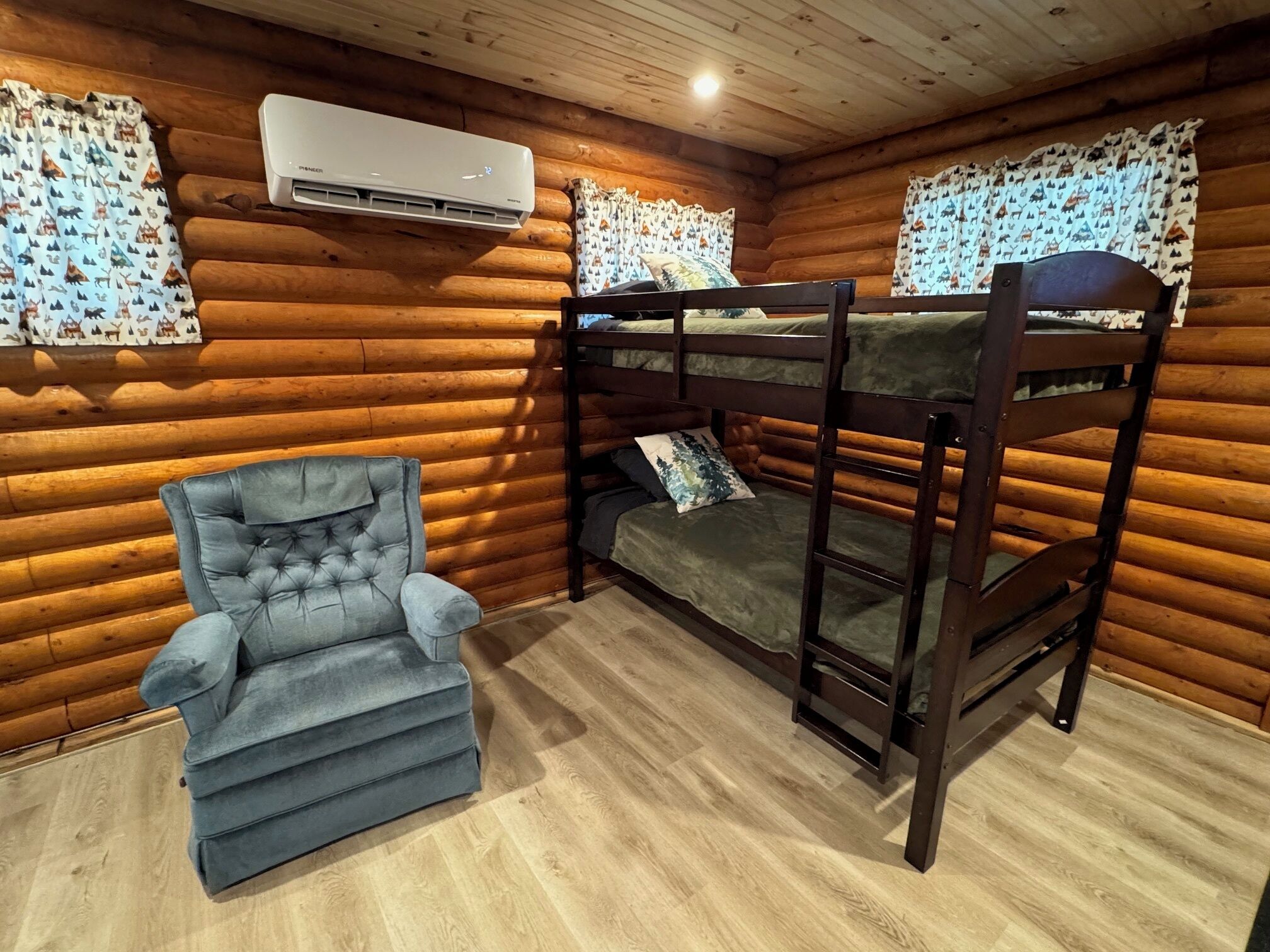 Habitació de cabana de fusta amb lliteres, un butac armchair tapissat i cortines estampades.