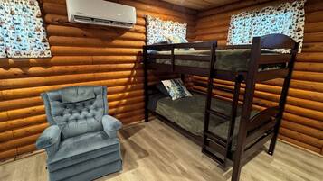Habitació de cabana de fusta amb lliteres, un butac armchair tapissat i cortines estampades.