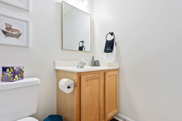 Un baño con lavamanos blanco, armarios de madera, un espejo y un dispensador de papel higiénico.