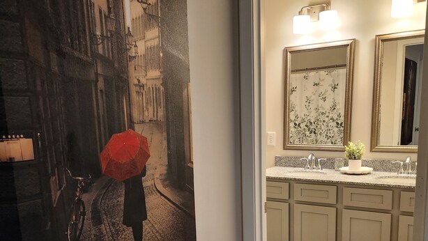A hallway leading to a bathroom with a large painting of a street scene, a bicycle, and an umbrella. - Newly Built Getaway! (Columbia)