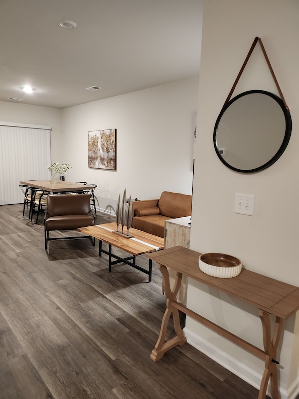 A modern living room with a dining area, a brown leather sofa, a wooden coffee table, and a round mirror on the wall.