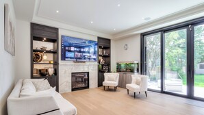Una sala de estar moderna con un sofá, sillones, una chimenea, un televisor y un ventanal grande.