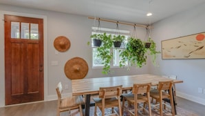 Een eetgedeelte met een houten tafel en stoelen, een hangplant en een deur met raam.