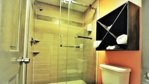 A bathroom with a glass-enclosed shower, a toilet, and a shelf with towels. - Scottish Inns & Suites Shenandoah Woodlands Mall (Shenandoah)