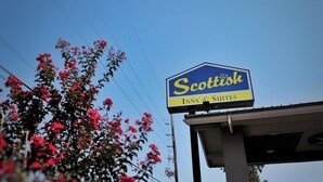 A sign for 'Scottish Inns & Suites' with a clear blue sky and red flowers in the background. - Scottish Inns & Suites Shenandoah Woodlands Mall (Shenandoah)