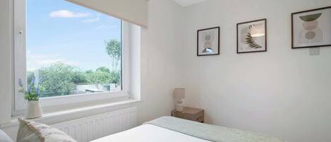 A bedroom with a bed, a bedside table, a lamp, and framed artwork on the wall.