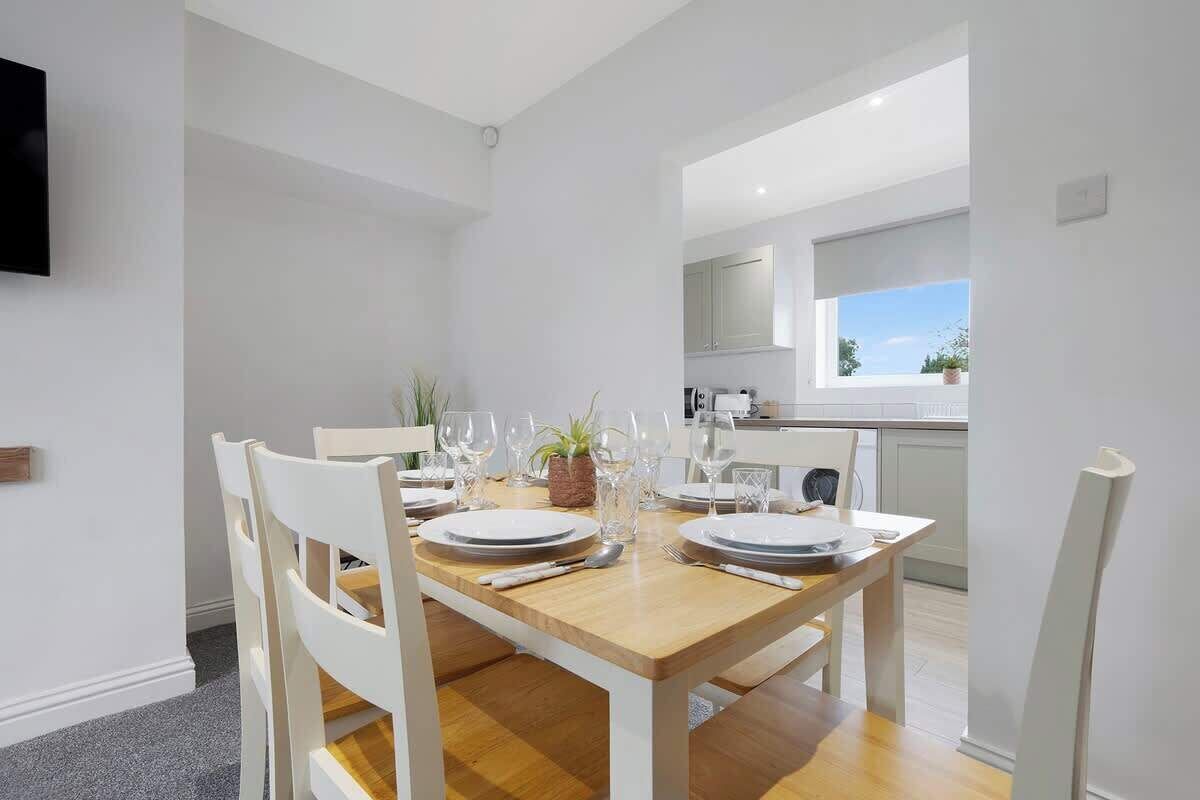 A dining area with a wooden table set for four, white chairs, and a view into the kitchen.