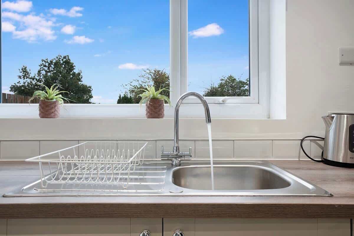 A kitchen with a stainless steel sink, a dish drying rack, and a window with a view of trees.