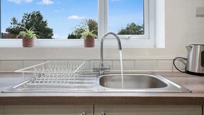 A kitchen with a stainless steel sink, a dish drying rack, and a window with a view of trees. - 3BR in County Durham with WiFi and Street Parking (Ludworth)