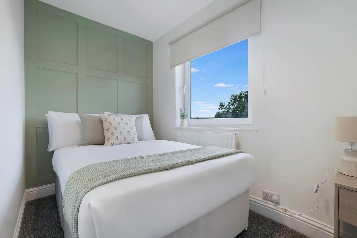 A bedroom with a bed, a window, a radiator, and a bedside table.