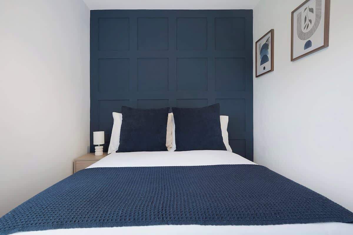 A bed with a dark headboard, white bedding, and a dark blue throw blanket.