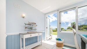 A room with a white and blue wall, a small table with a decorative fish wall art, a basket, and a view through a glass door. - Crystal Cove Beachfront Pool Tennis (St. Thomas)