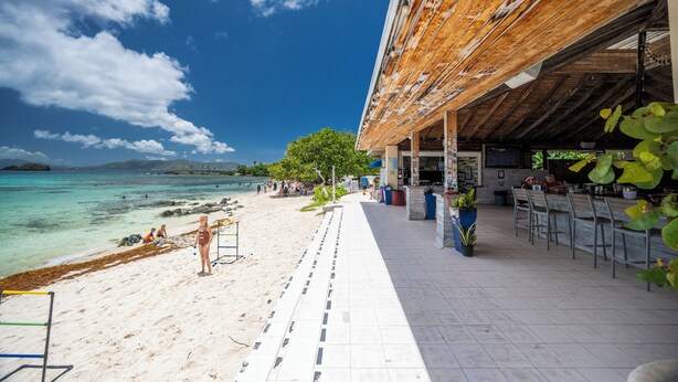 A beachside restaurant with outdoor seating, a view of the ocean, and a covered area with a bar. - Crystal Cove Beachfront Pool Tennis (St. Thomas)