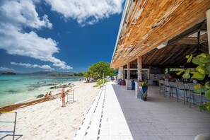 A beachside restaurant with outdoor seating, a view of the ocean, and a covered area with a bar. - Crystal Cove Beachfront Pool Tennis (St. Thomas)