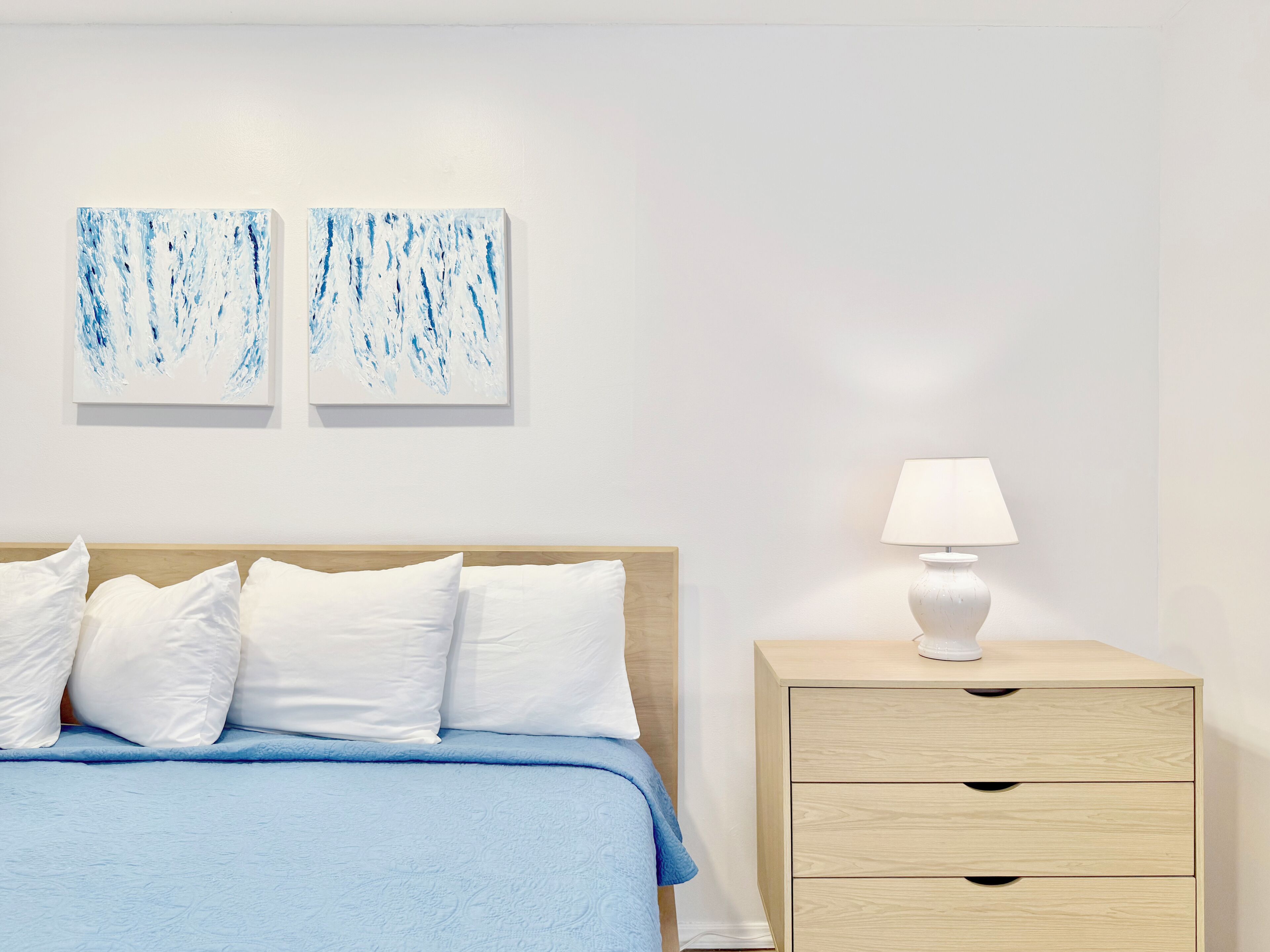 Une chambre d’hôtel avec un lit, une table de chevet avec une lampe et deux tableaux abstraits accrochés au mur.