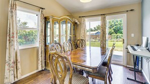 Une salle à manger avec une table en bois, six chaises, un piano et une vue sur l’extérieur.