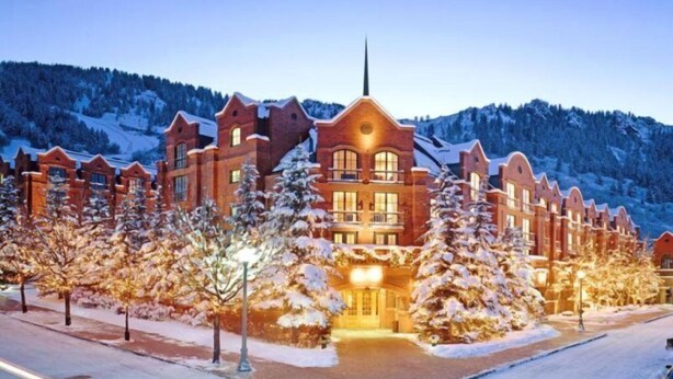 A large, multi-story hotel with a symmetrical facade, snow-covered trees, and a mountainous backdrop.