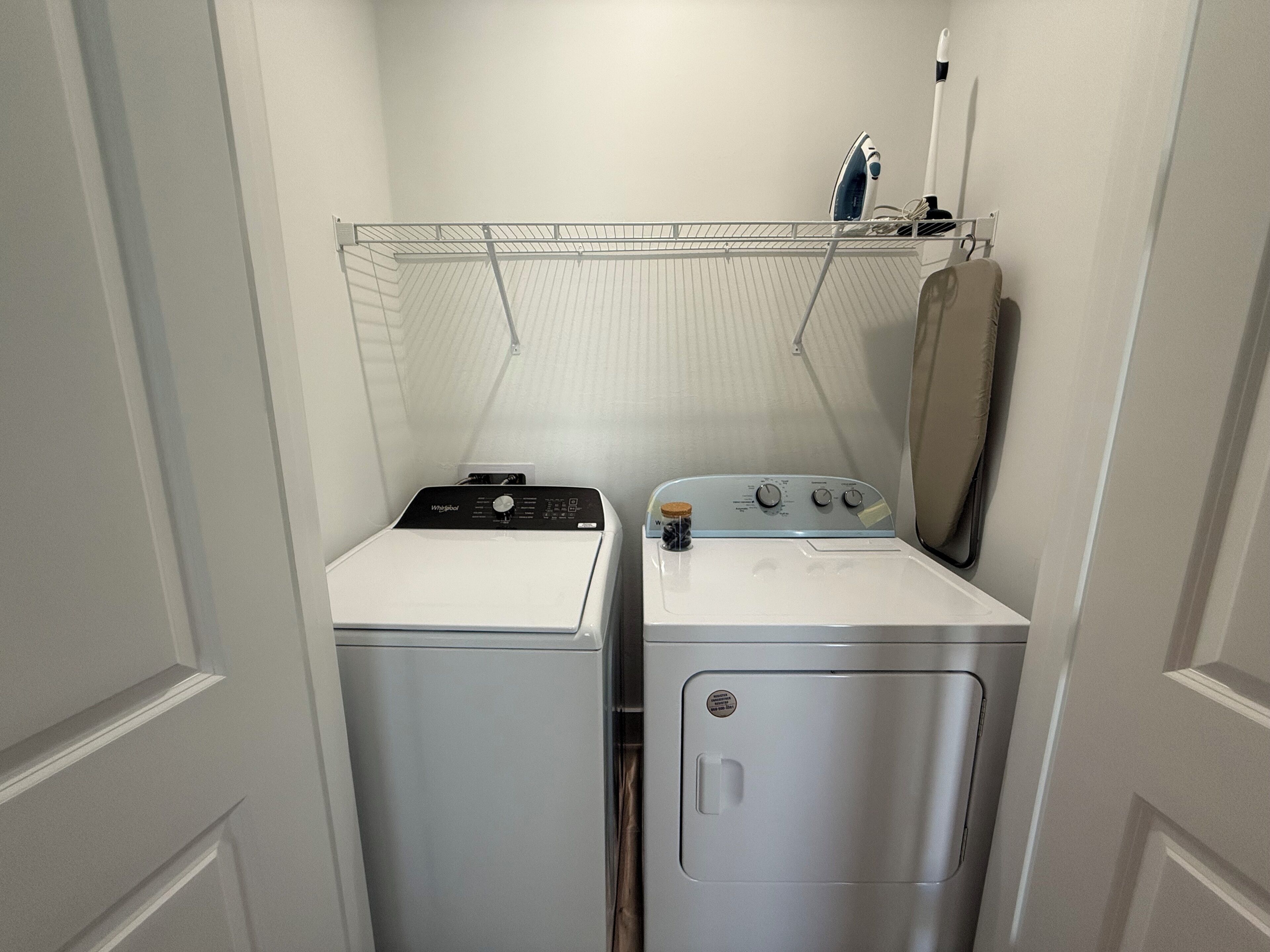 A compact laundry room with a front-loading washer and dryer, a drying rack, and a mirror above the dryer.