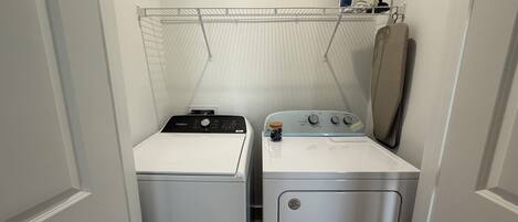 A compact laundry room with a front-loading washer and dryer, a drying rack, and a mirror above the dryer.