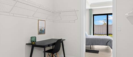 A modern room with a desk, chair, and a bed. There is a window with a view of the sky and a door leading to another room.