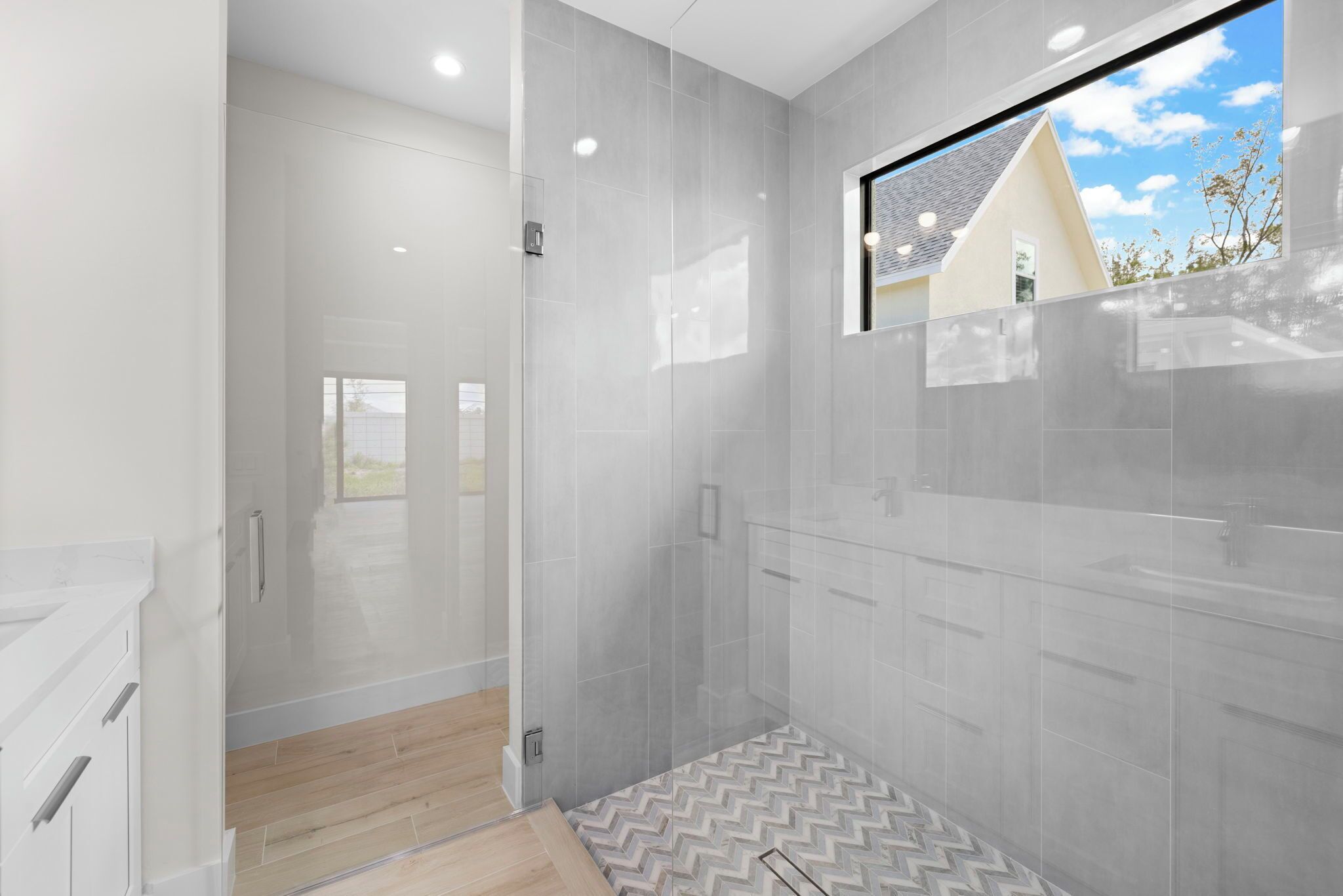 A modern bathroom with a glass shower enclosure, a large mirror, and a view of the outside.