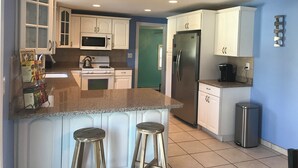 A kitchen with white cabinets, a stainless steel refrigerator, a microwave, a stove, and two stools.