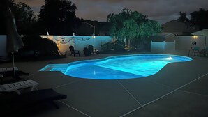 A backyard with a swimming pool, lounge chairs, and a hammock.