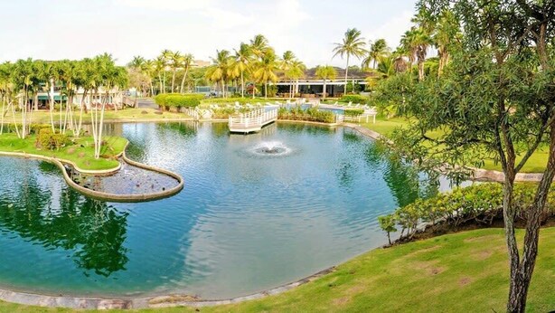 A large, circular water feature with a fountain in the center, surrounded by well-maintained grass and palm trees. - Quaint villa Beach access Elina (Sabana)