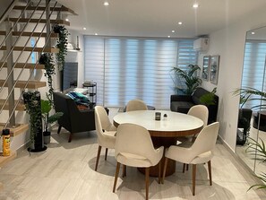 Een moderne eetruimte met een ronde tafel, stoelen, een trap en potplanten.