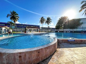 Una piscina con una fontana, circondata da palme e un edificio con tetto blu.
