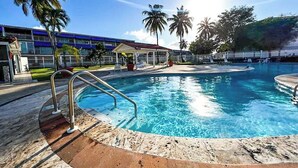 A swimming pool with a clear blue water, surrounded by a tiled deck and palm trees. - 3BR Villa Mira  short stroll from the Beach & Pool (Dorado)