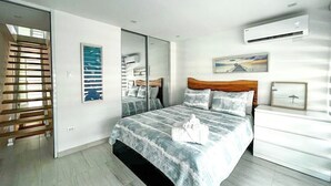 A modern bedroom with a large bed, a wooden headboard, a nightstand, and a wall-mounted air conditioner. - 3BR Villa Mira  short stroll from the Beach & Pool (Dorado)