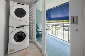 A laundry room with two Whirlpool washing machines, a sliding glass door leading to a balcony with a blue awning.