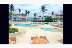 A resort pool area with two pools, palm trees, and a building with a red roof in the background.