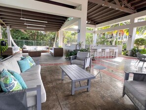 Une terrasse extérieure couverte, aménagée avec des sièges, notamment un canapé et des fauteuils, ainsi qu’une table.