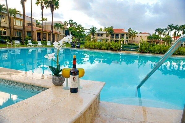 Une piscine avec des chaises longues, une bouteille de vin et des plantes tropicales.
