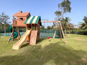 A wooden play structure with a slide and swings in a grassy outdoor area.