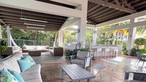 Ein überdachter Außenbereich mit einer Terrasse, ausgestattet mit Sitzgelegenheiten, darunter Sofas und Stühle, sowie einem Couchtisch.